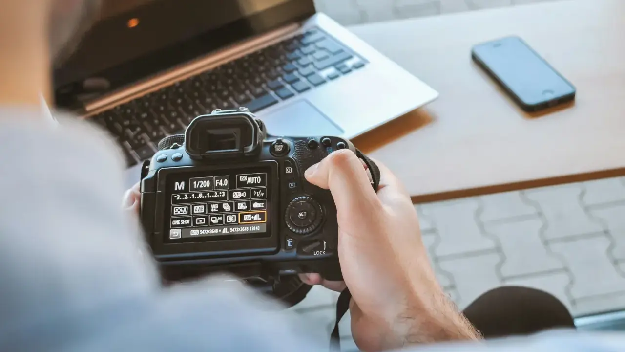 Una foto sera con una fotocamera reflex, un laptop e uno smartphone sul tavolo.