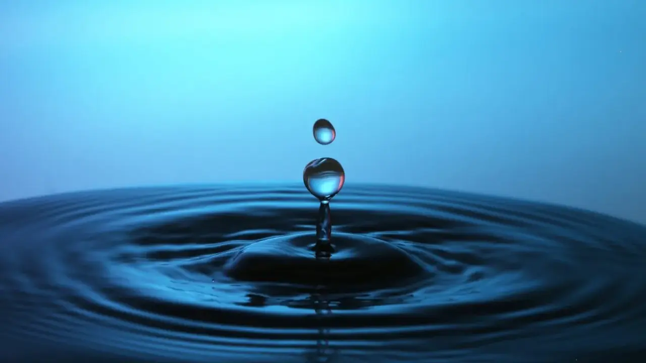 Momento magico nel fotografare gocce d'acqua: una cade, l'altra la segue, creando onde perfette su uno sfondo blu.