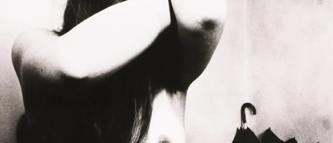 Un corpo femminile in primo piano, con le braccia sollevate, in uno stile che ricorda Bill Brandt. Un ombrello nero è appeso sullo sfondo.