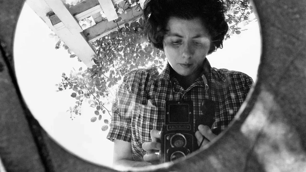 La fotografa famosa si riflette in uno specchio, impugnando la sua macchina fotografica.