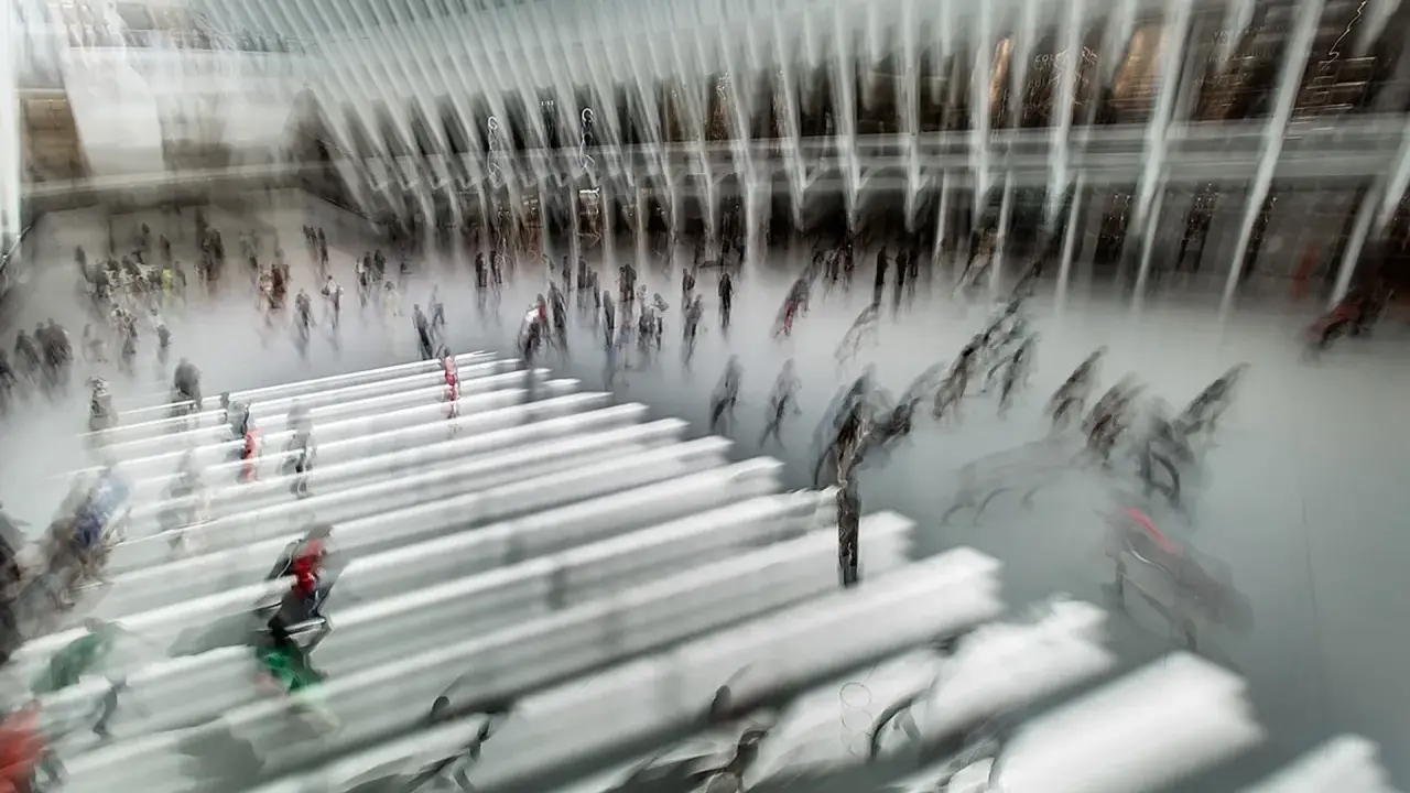 Persone in movimento in una grande hall moderna, con un forte effetto mosso che crea un senso di dinamismo e velocità.