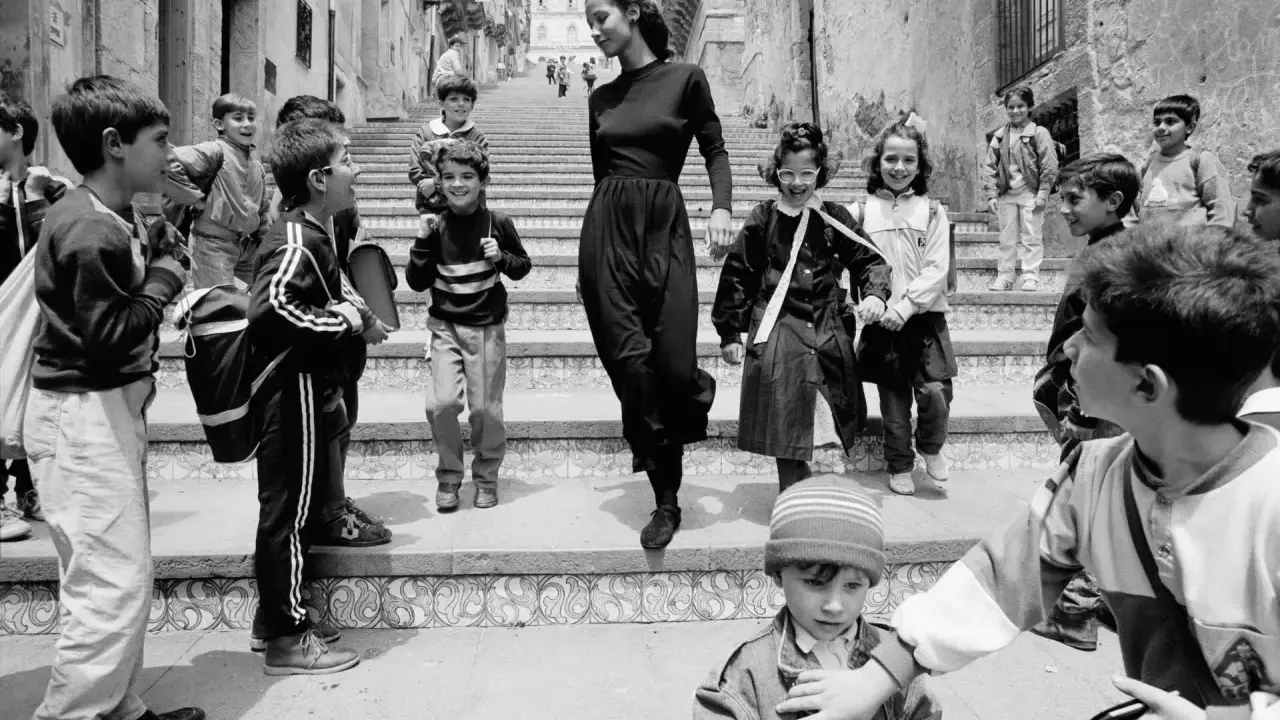Bambini con zaini scendono una scalinata, accompagnati da una donna elegante. Un'istantanea che cattura la vivacità di queste fotografie famose.