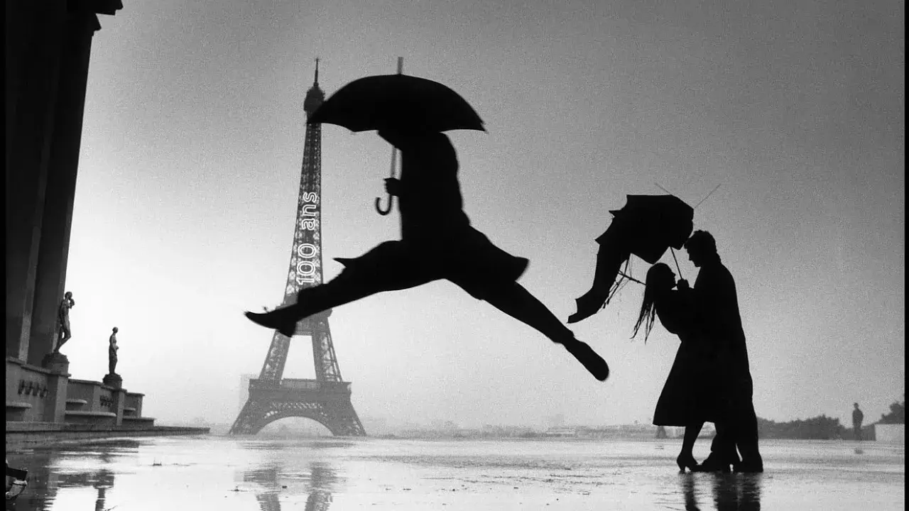 Parigi piovosa: un ballerino salta, una coppia si abbraccia sotto un ombrello. Un'iconica scena che ricorda i grandi fotografi famosi.