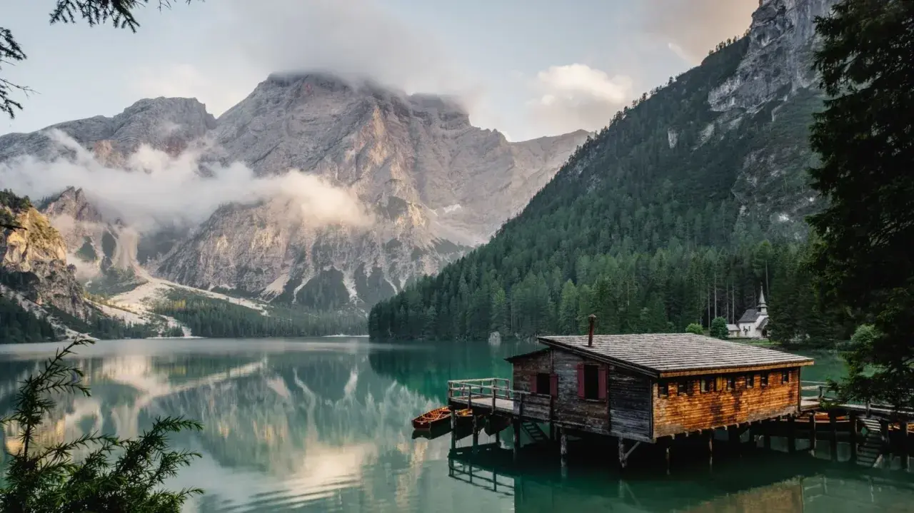 Un rifugio di legno su un lago alpino, perfetto per fotografare paesaggi mozzafiato. Montagne imponenti e foreste verdi incorniciano la scena.