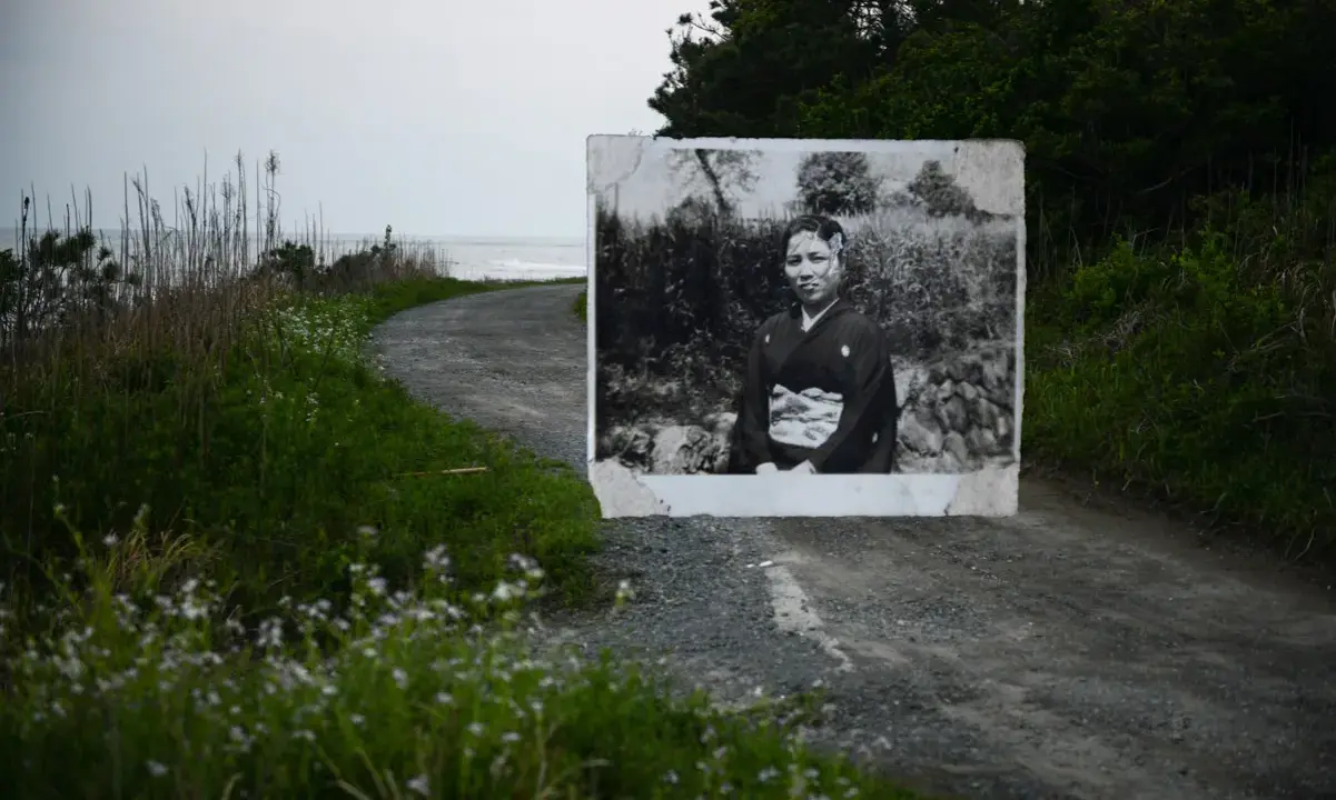 Un ritratto di una donna in kimono, evocativo dei fotografi giapponesi contemporanei, appare su una strada sterrata che conduce al mare.