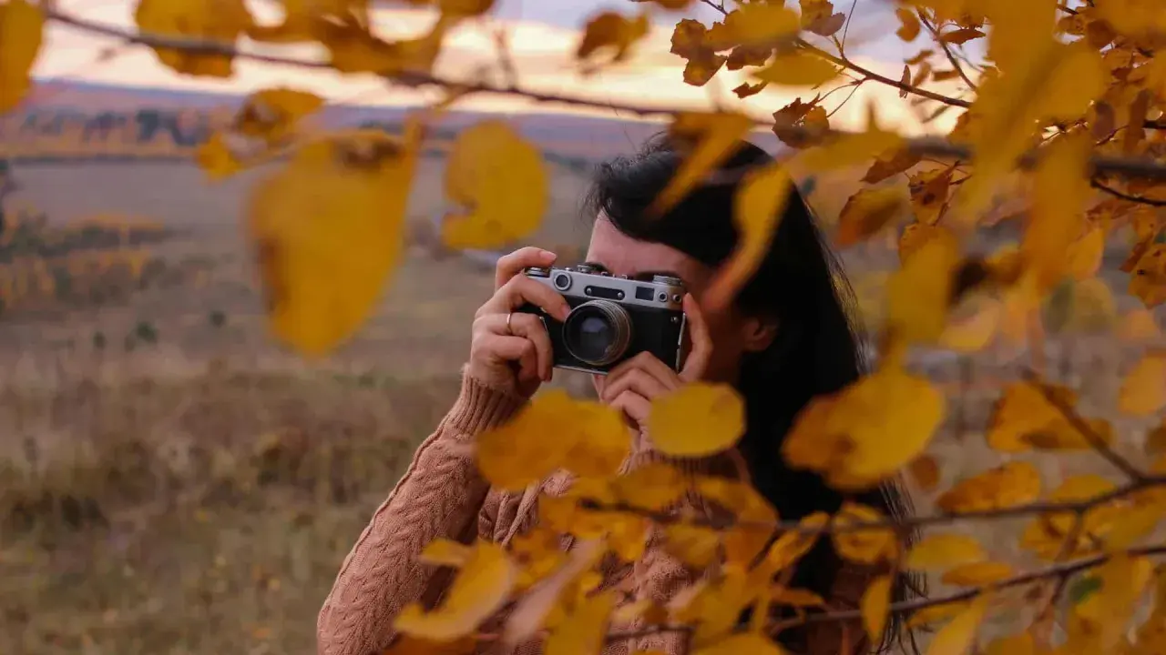 Ragazza con macchina fotografica vintage, tra foglie autunnali. Un tutorial fotografia per catturare la magia della natura.