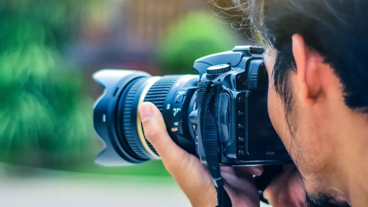 Un fotografo cattura un momento con la sua macchina fotografica reflex, il sole illumina i suoi capelli mossi.