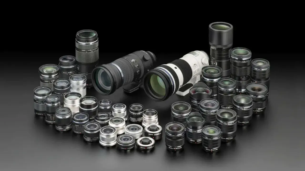 Una vasta collezione di obiettivi fotografici, dai più compatti ai teleobiettivi professionali, disposti su sfondo nero.