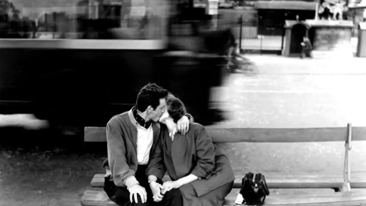 Un bacio rubato tra le opere di Robert Doisneau, un momento sospeso nel tempo con un tram sfocato sullo sfondo.