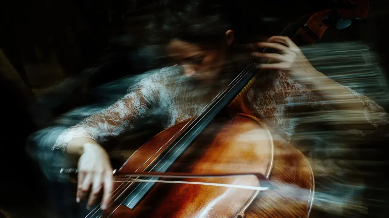 Donna suona il violoncello con un effetto mosso, quasi etereo. Un esempio di come fare foto mosse con iPhone per un risultato artistico.