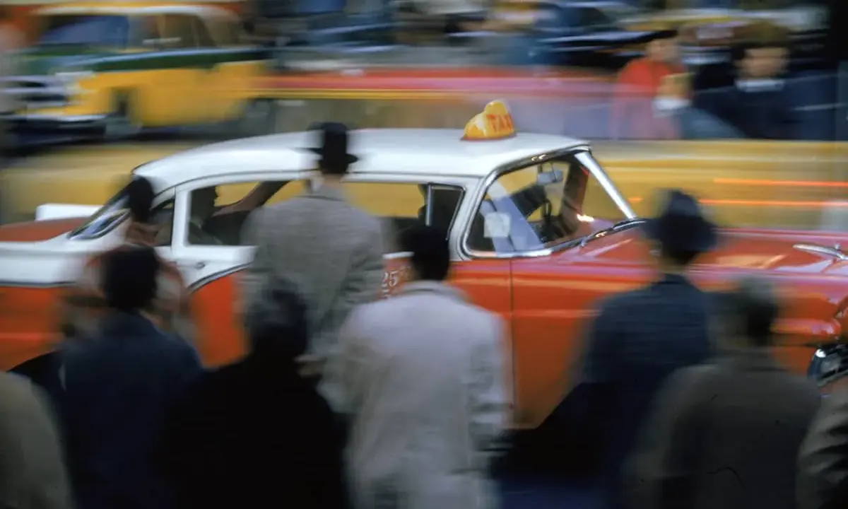 Un taxi rosso e bianco sfreccia in una strada trafficata, un'istantanea che cattura l'essenza di quando nasce la fotografia a colori.