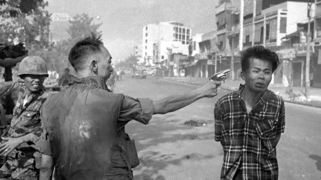 Un soldato punta una pistola alla testa di un uomo in un crudo reportage di guerra. La scena è ambientata in una strada urbana.