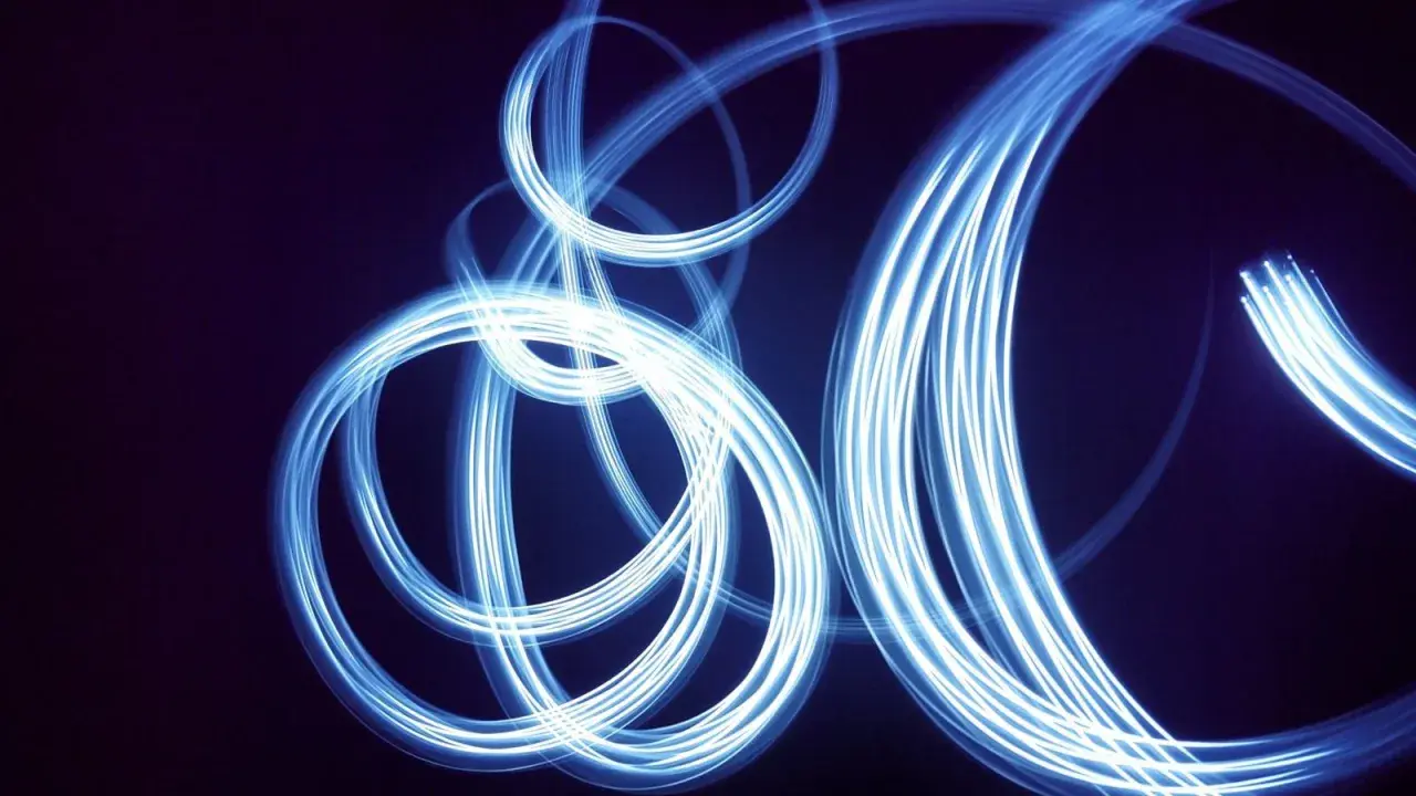 Light painting still life con fili di luce blu che danzano su sfondo scuro, creando un effetto etereo e astratto.