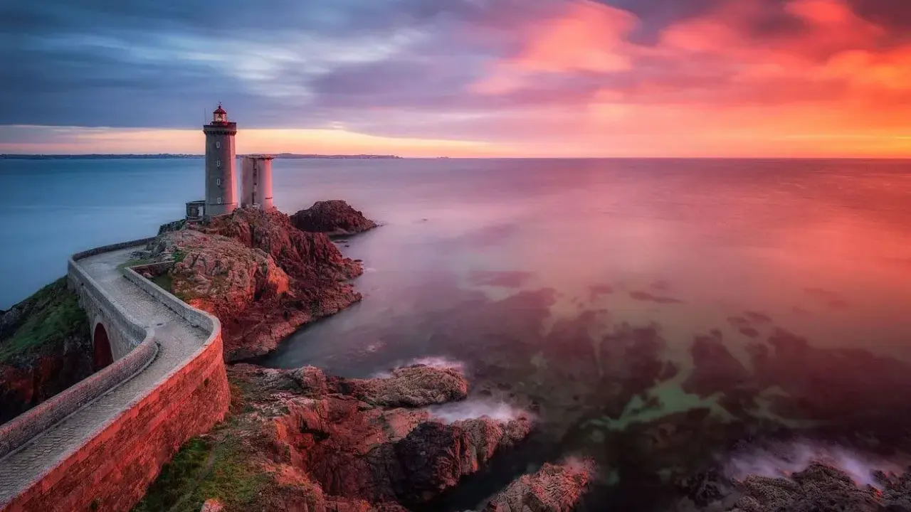 Faro su scogliera al tramonto, con cielo infuocato e mare calmo. Un filtro polarizzatore a cosa serve? A rendere i colori più vividi e il cielo più profondo.