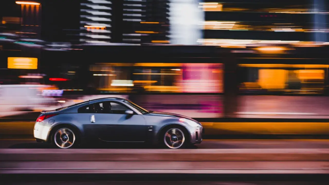 Auto sportiva grigia in movimento notturno, con luci sfocate sullo sfondo che creano un effetto di panning.