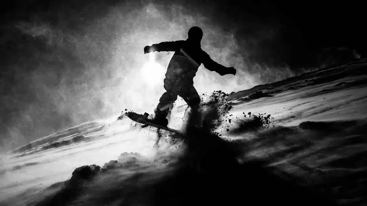 Snowboarder in silhouette, sollevando neve in una foto con ombre drammatiche.