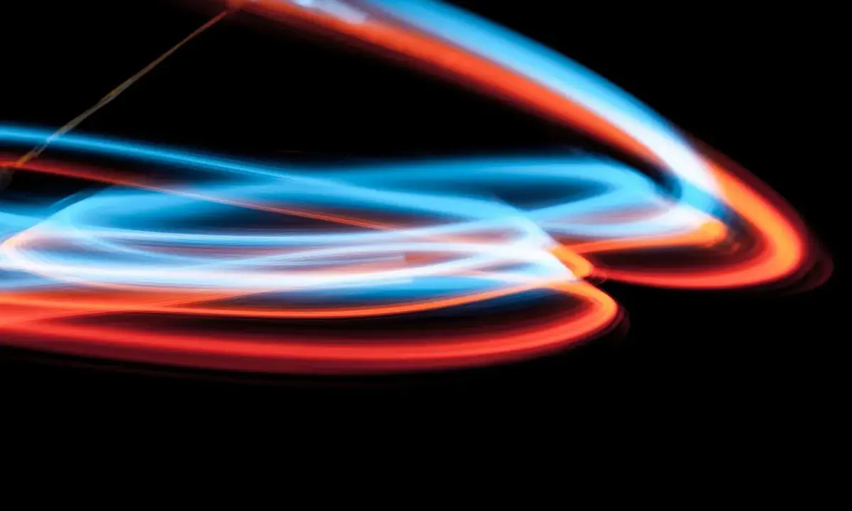 Linee luminose blu e arancioni danzano su sfondo nero, un'esplosione di **light painting** astratto.