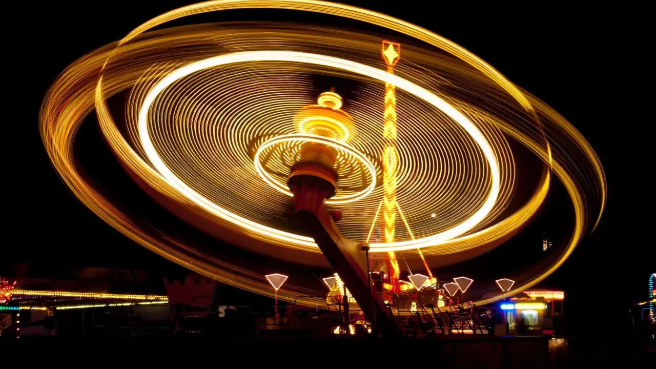 Effetto spirale di luci dorate su un'attrazione da luna park in movimento, catturata con una **panning shot** notturna.