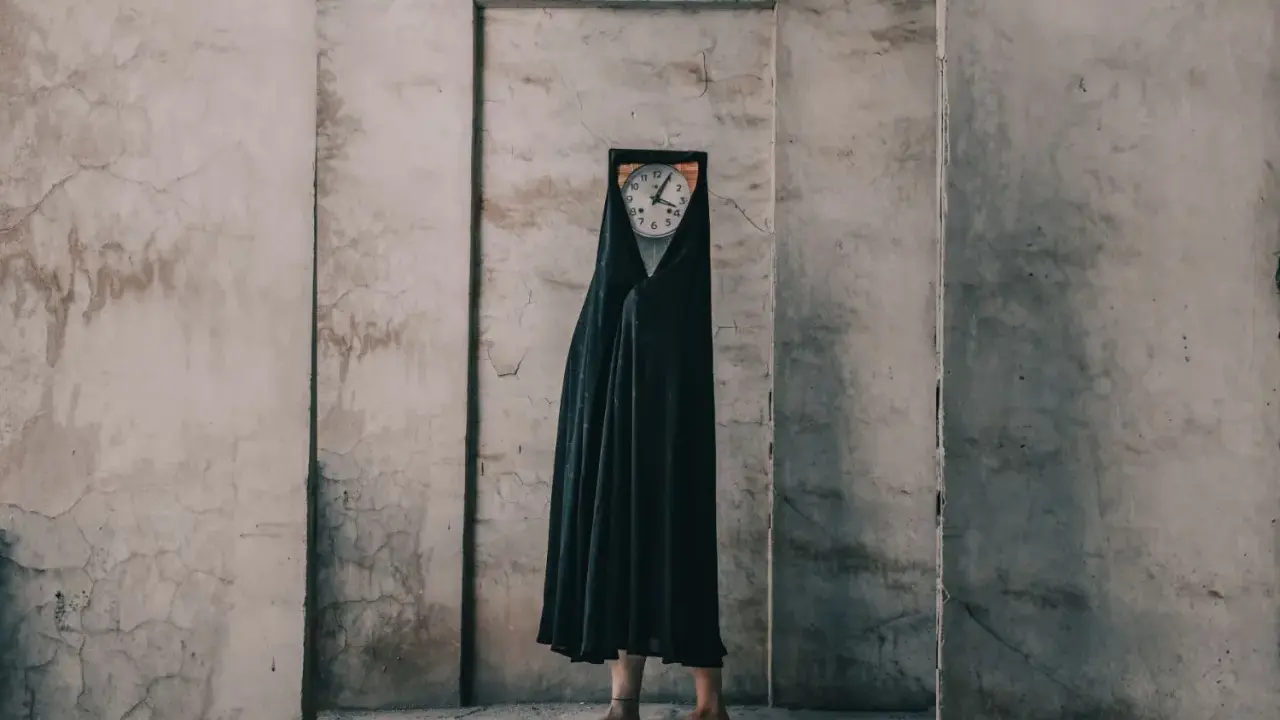 Figura con un orologio al posto della testa, avvolta in un drappo nero, in un ambiente spoglio. Un'opera che evoca i fotografi surrealisti contemporanei.