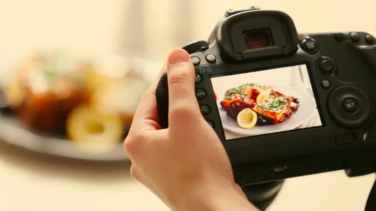 Mano che tiene una fotocamera per fare food photography di un piatto invitante con limone e erbe aromatiche.