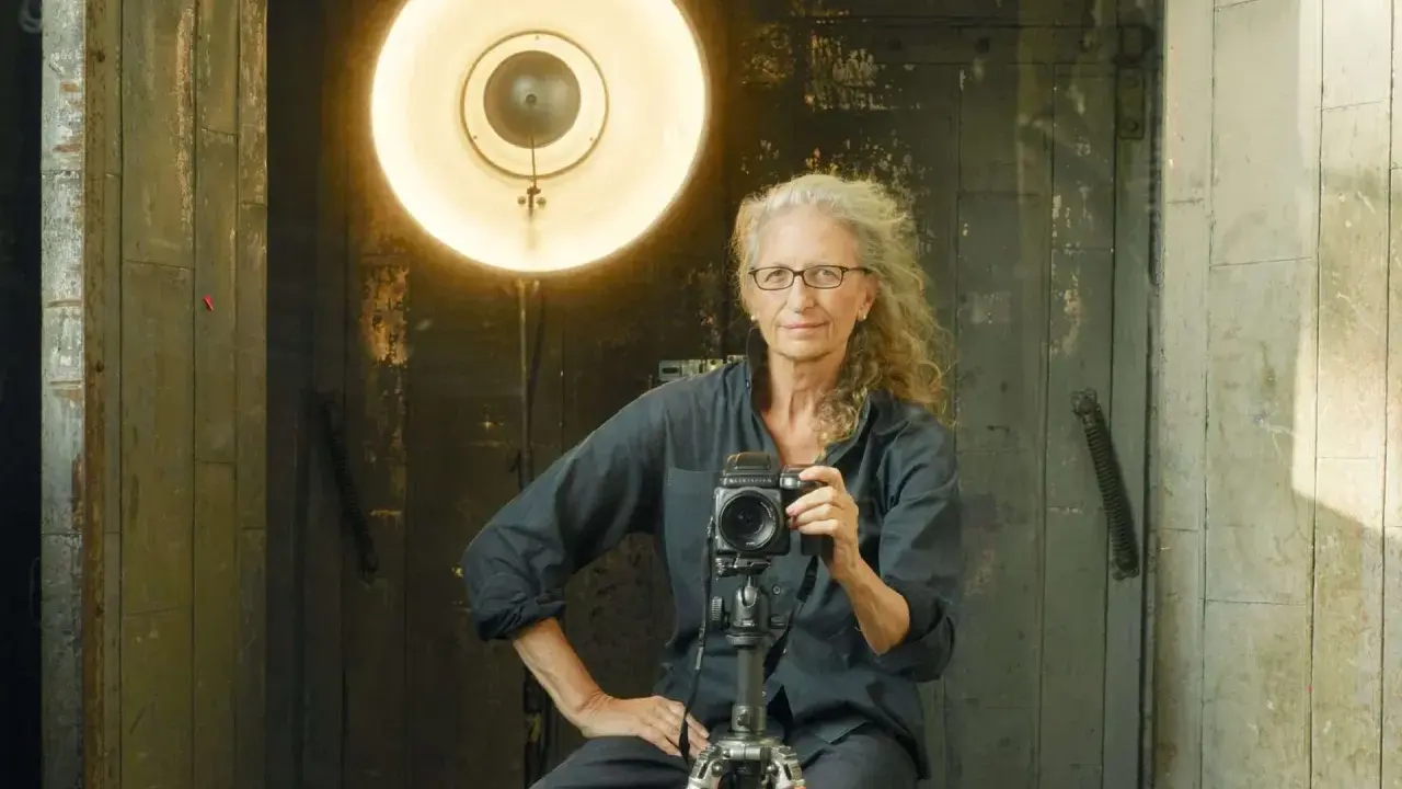 Annie Leibovitz foto: la celebre fotografa con la sua macchina fotografica, illuminata da un grande riflettore.