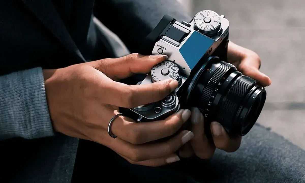 Mani che regolano i quadranti di una fotocamera, con un anello al dito. Immagine fotografica.