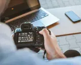 Una foto sera con una fotocamera reflex, un laptop e uno smartphone sul tavolo.
