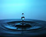 Momento magico nel fotografare gocce d'acqua: una cade, l'altra la segue, creando onde perfette su uno sfondo blu.