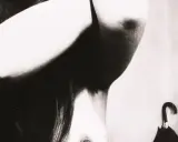 Un corpo femminile in primo piano, con le braccia sollevate, in uno stile che ricorda Bill Brandt. Un ombrello nero è appeso sullo sfondo.