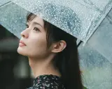 Una giovane donna con un ombrello trasparente osserva il cielo, la pioggia cade. Foto sotto la pioggia.