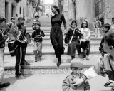 Bambini con zaini scendono una scalinata, accompagnati da una donna elegante. Un'istantanea che cattura la vivacità di queste fotografie famose.