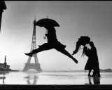 Parigi piovosa: un ballerino salta, una coppia si abbraccia sotto un ombrello. Un'iconica scena che ricorda i grandi fotografi famosi.
