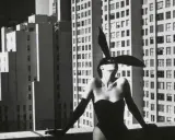 Iconica immagine di Helmut Newton: una donna con orecchie da coniglio e un corsetto nero posa su un tetto, con grattacieli sullo sfondo.