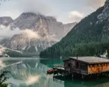 Un rifugio di legno su un lago alpino, perfetto per fotografare paesaggi mozzafiato. Montagne imponenti e foreste verdi incorniciano la scena.