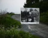 Un ritratto di una donna in kimono, evocativo dei fotografi giapponesi contemporanei, appare su una strada sterrata che conduce al mare.