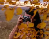 Ragazza con macchina fotografica vintage, tra foglie autunnali. Un tutorial fotografia per catturare la magia della natura.
