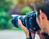 Un fotografo cattura un momento con la sua macchina fotografica reflex, il sole illumina i suoi capelli mossi.