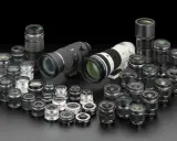 Una vasta collezione di obiettivi fotografici, dai più compatti ai teleobiettivi professionali, disposti su sfondo nero.