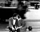 Un bacio rubato tra le opere di Robert Doisneau, un momento sospeso nel tempo con un tram sfocato sullo sfondo.