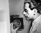Man Ray, con la sua mano, manipola un oggetto che ricorda i suoi celebri rayogrammi, creando un'ombra enigmatica.