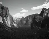 Iconici paesaggi di Yosemite, immortalati da fotografi famosi. Maestose pareti rocciose, una cascata e una fitta foresta sotto un cielo nuvoloso.