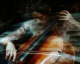 Donna suona il violoncello con un effetto mosso, quasi etereo. Un esempio di come fare foto mosse con iPhone per un risultato artistico.