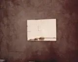 Specchio riflette lavandini in un bagno spoglio, un'immagine che evoca la poetica di Luigi Ghirri.