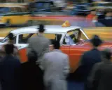 Un taxi rosso e bianco sfreccia in una strada trafficata, un'istantanea che cattura l'essenza di quando nasce la fotografia a colori.
