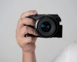 Mano che tiene una fotocamera compatta, mostrando le parti macchina fotografica come l'obiettivo e il corpo nero.