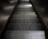 Scale mobili con un suggestivo **effetto moiré** creato dalle luci che si riflettono sui gradini metallici.