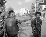 Un soldato punta una pistola alla testa di un uomo in un crudo reportage di guerra. La scena è ambientata in una strada urbana.