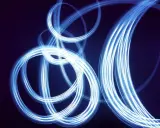 Light painting still life con fili di luce blu che danzano su sfondo scuro, creando un effetto etereo e astratto.