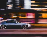 Auto sportiva grigia in movimento notturno, con luci sfocate sullo sfondo che creano un effetto di panning.