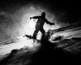 Snowboarder in silhouette, sollevando neve in una foto con ombre drammatiche.